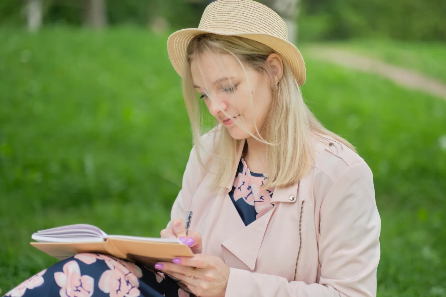 Girl with pen writing on notebook on grass